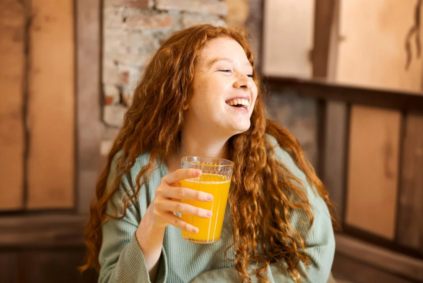 Frau mit roten Haaren trinkt O-Saft Glas und lacht
