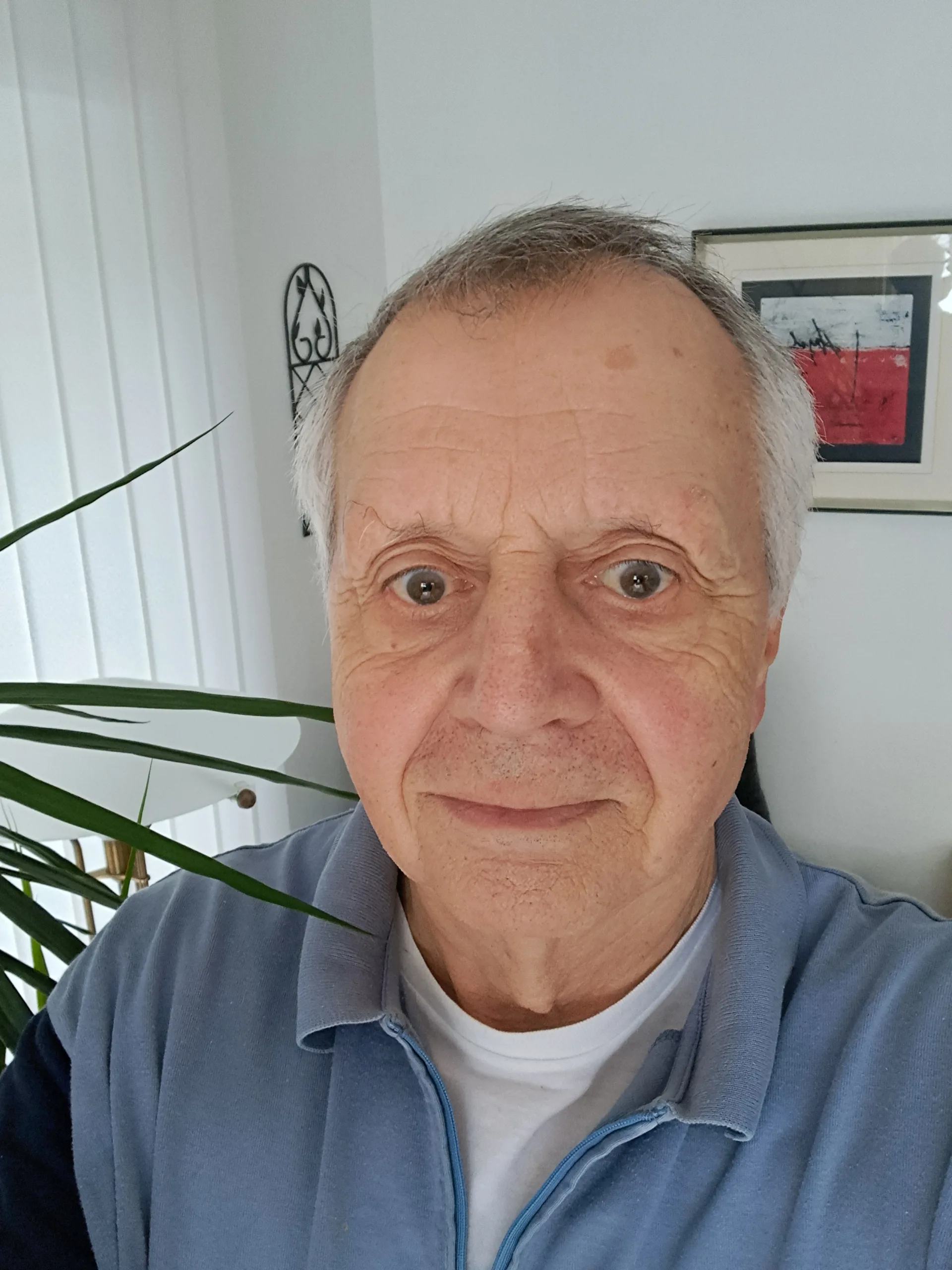 Originalbild von Hugh, der in seinem Wohnzimmer steht und ausdruckslos in die Kamera blickt